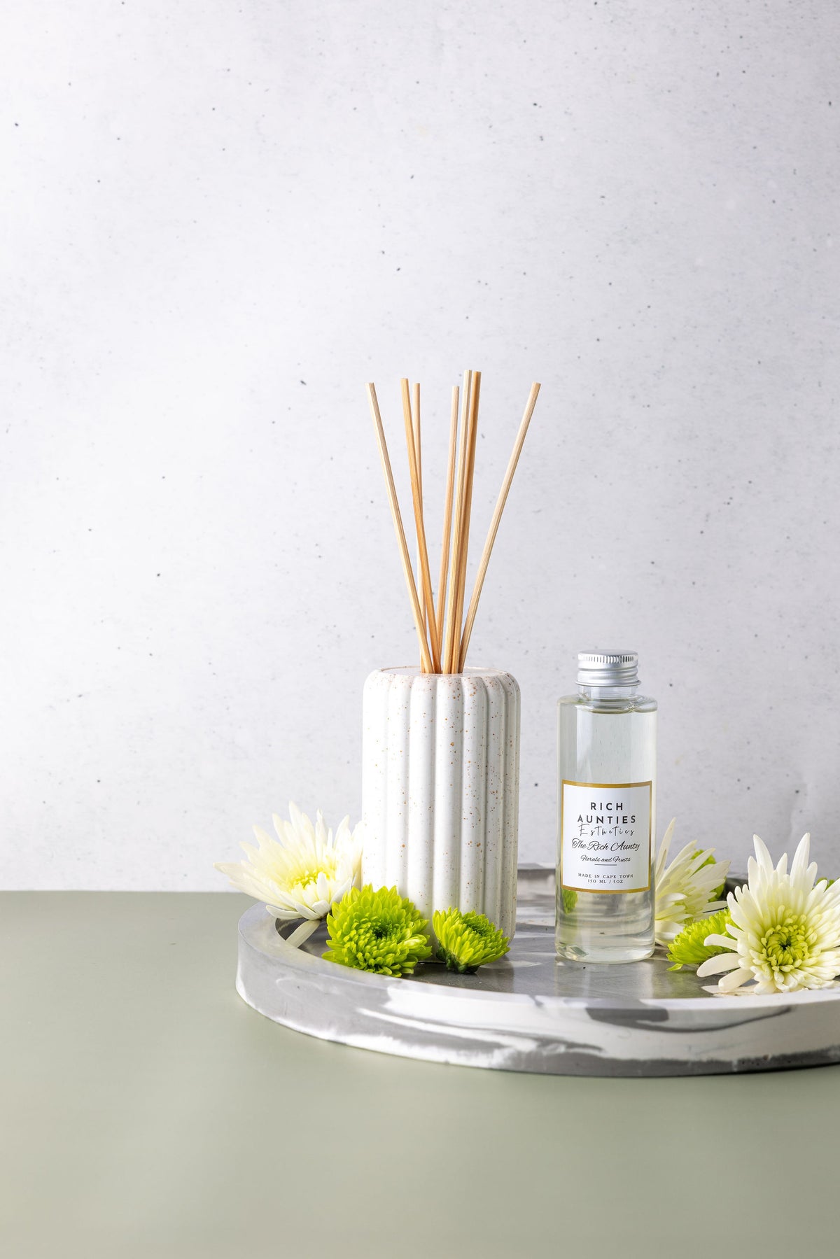 Diffuser with reeds and a bottle on a tray with flowers on a light background