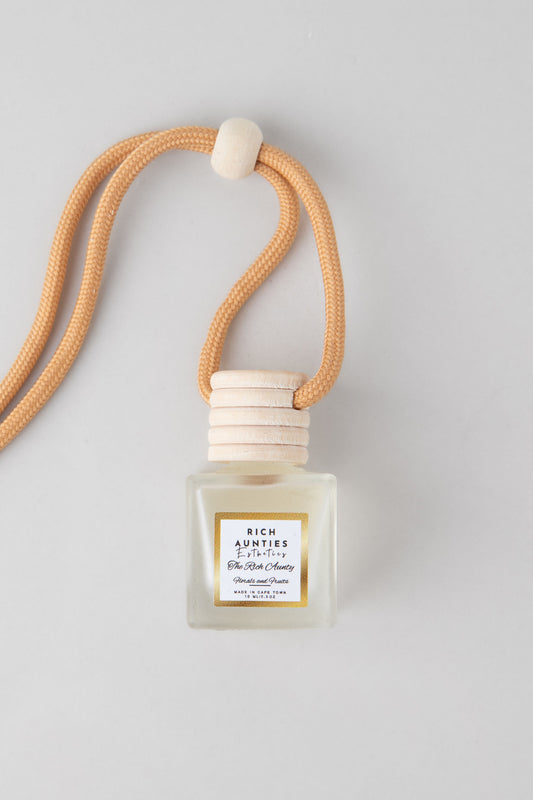A square-shaped car diffuser with a clear liquid and blackberry, pear, and orange fragrance notes, attached to a beige Reed diffuser with a white cap and a label, presented on a white background.