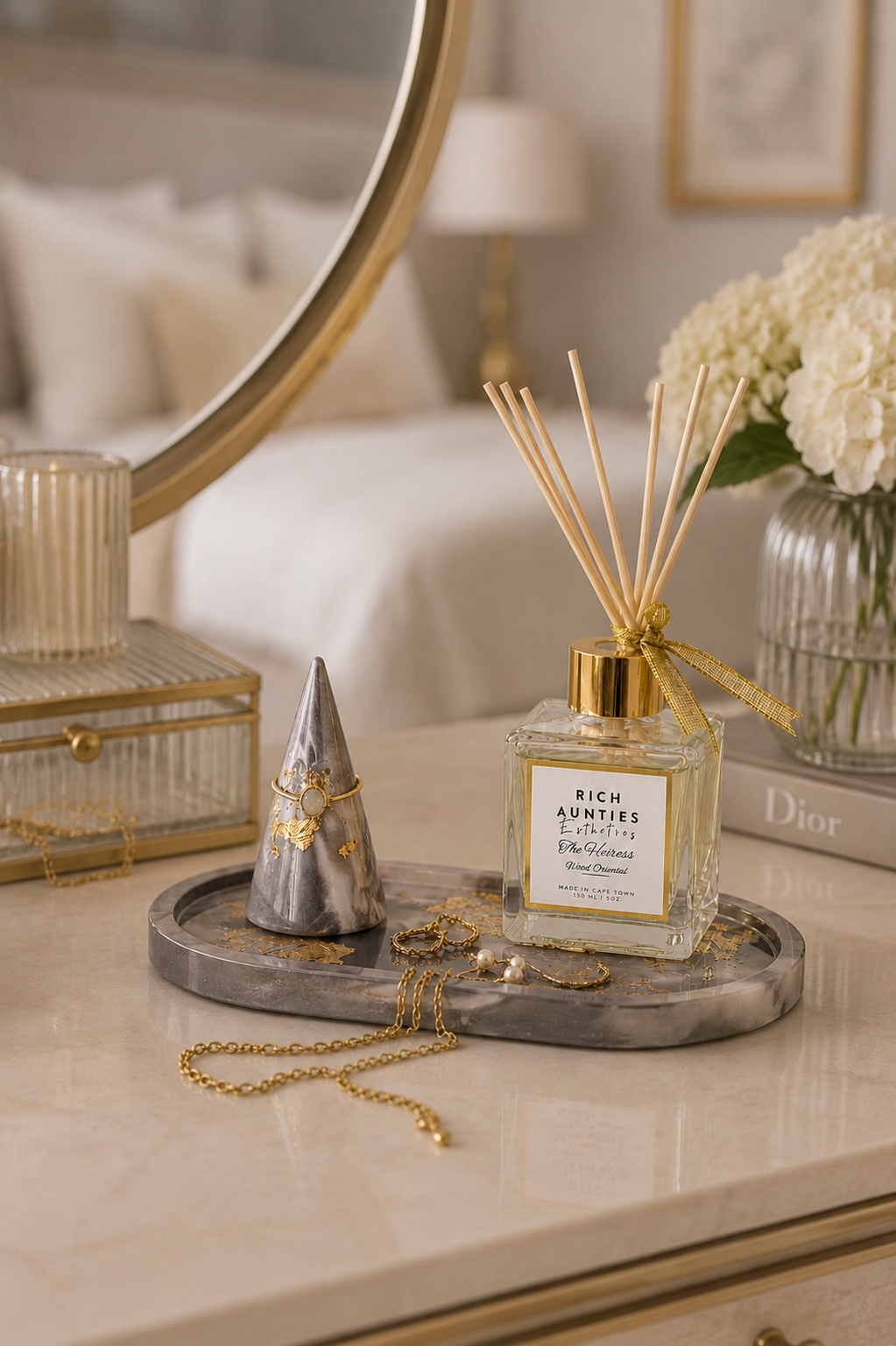 Luxury reed diffuser for home fragrance styled on a marble tray with jewelry and white hydrangeas in an elegant bedroom.
