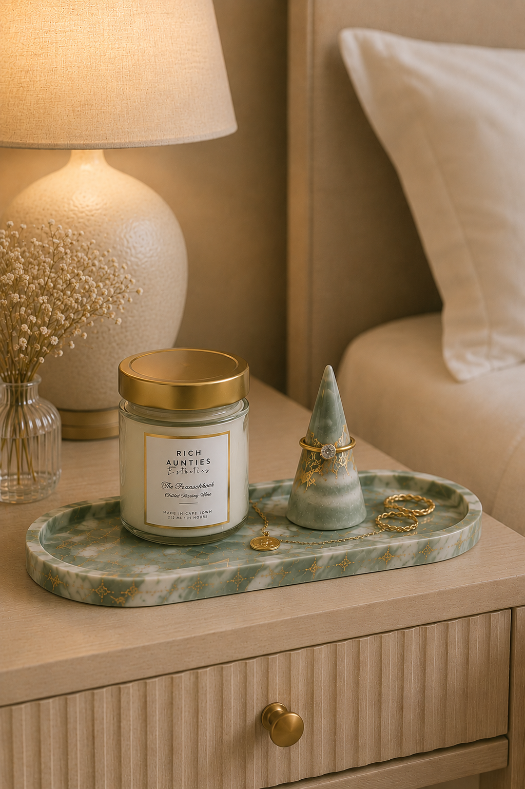 The Franschhoek Scented Candle with gold lid on a green marble gold leaf tray next to a lamp and decorative items on a nightstand.