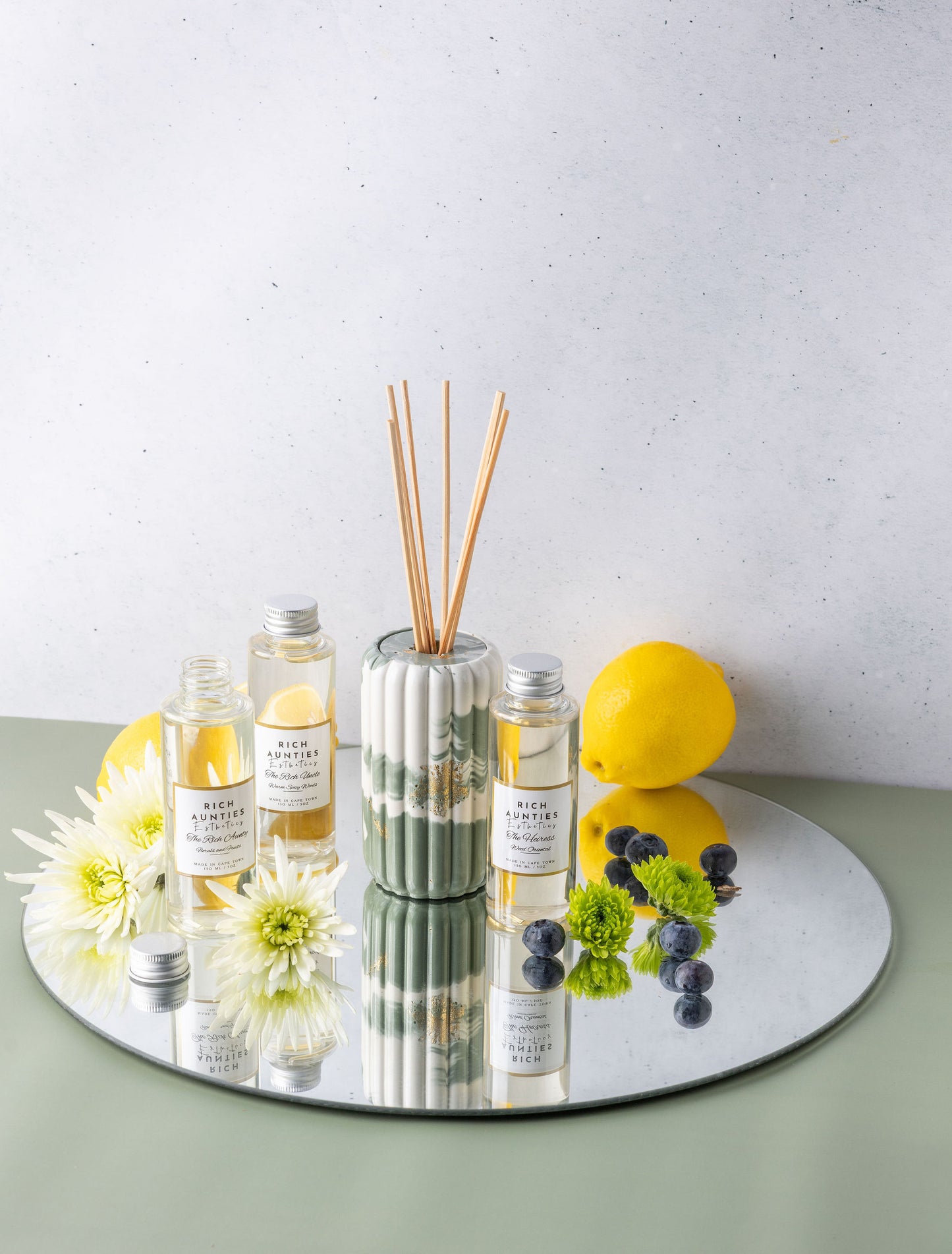 Diffuser with reeds, bottles, and decorative items on a reflective surface with a light background
