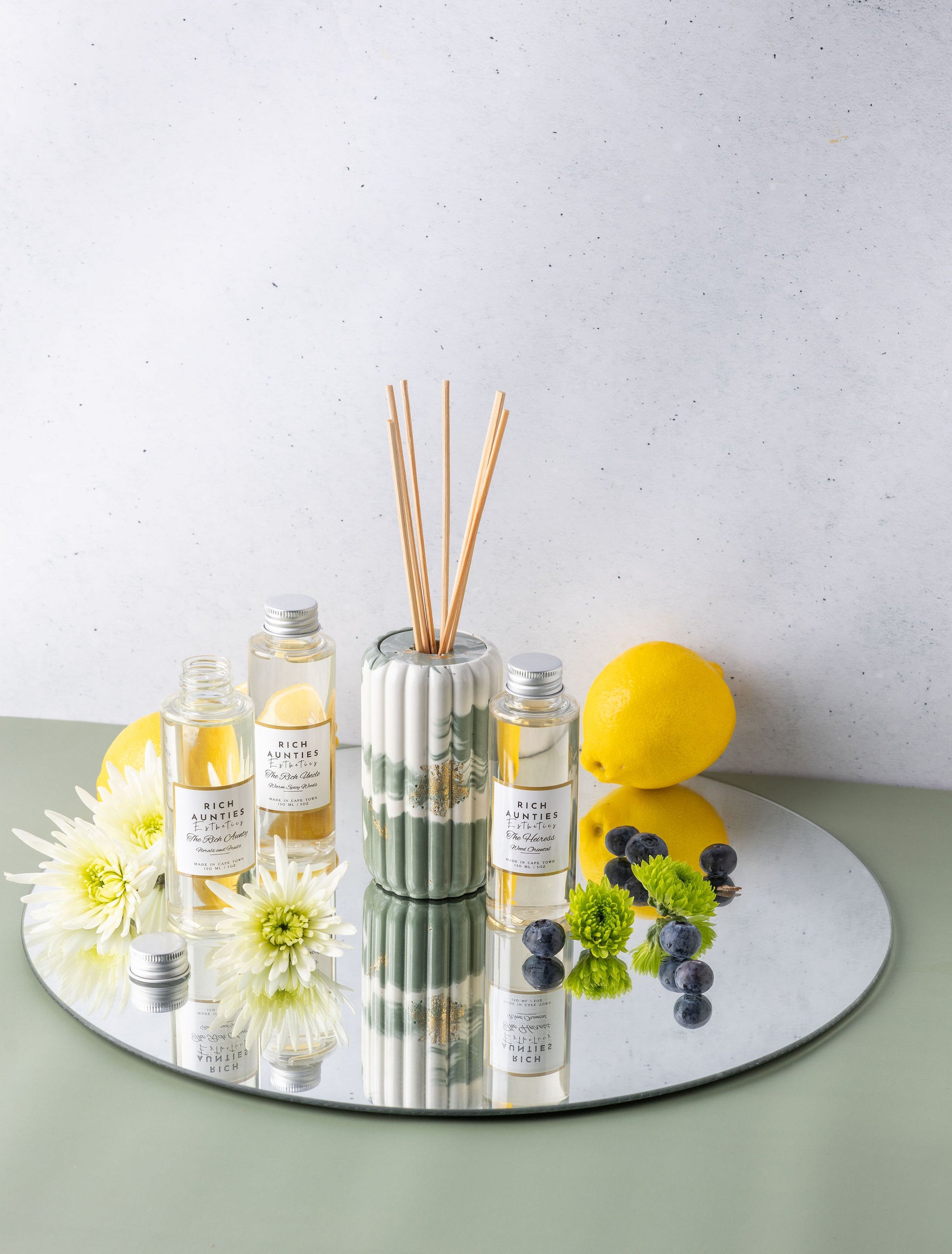 Diffuser with reeds, bottles, and decorative items on a reflective surface with a light background