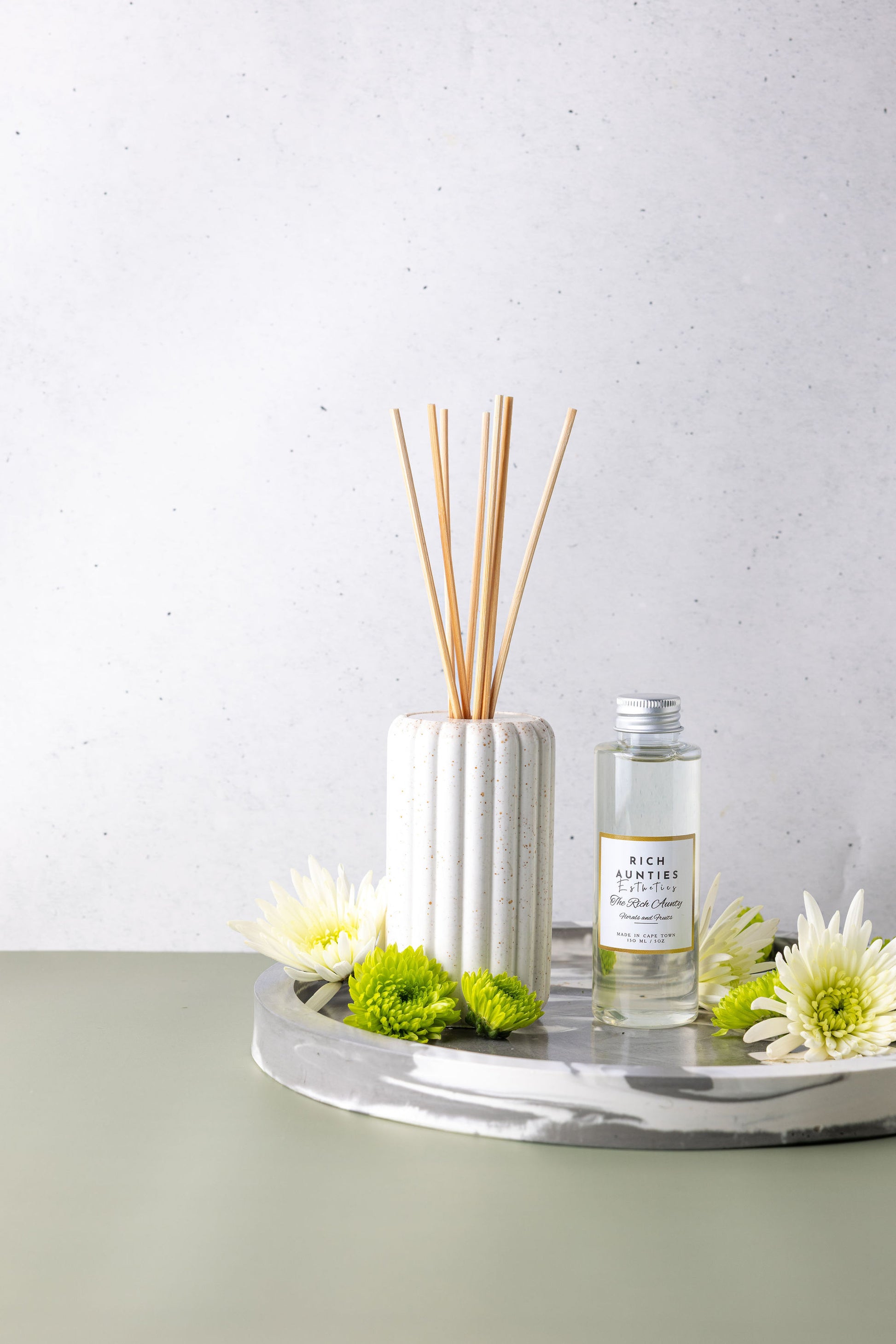 Diffuser with reeds and a bottle on a tray with flowers on a light background